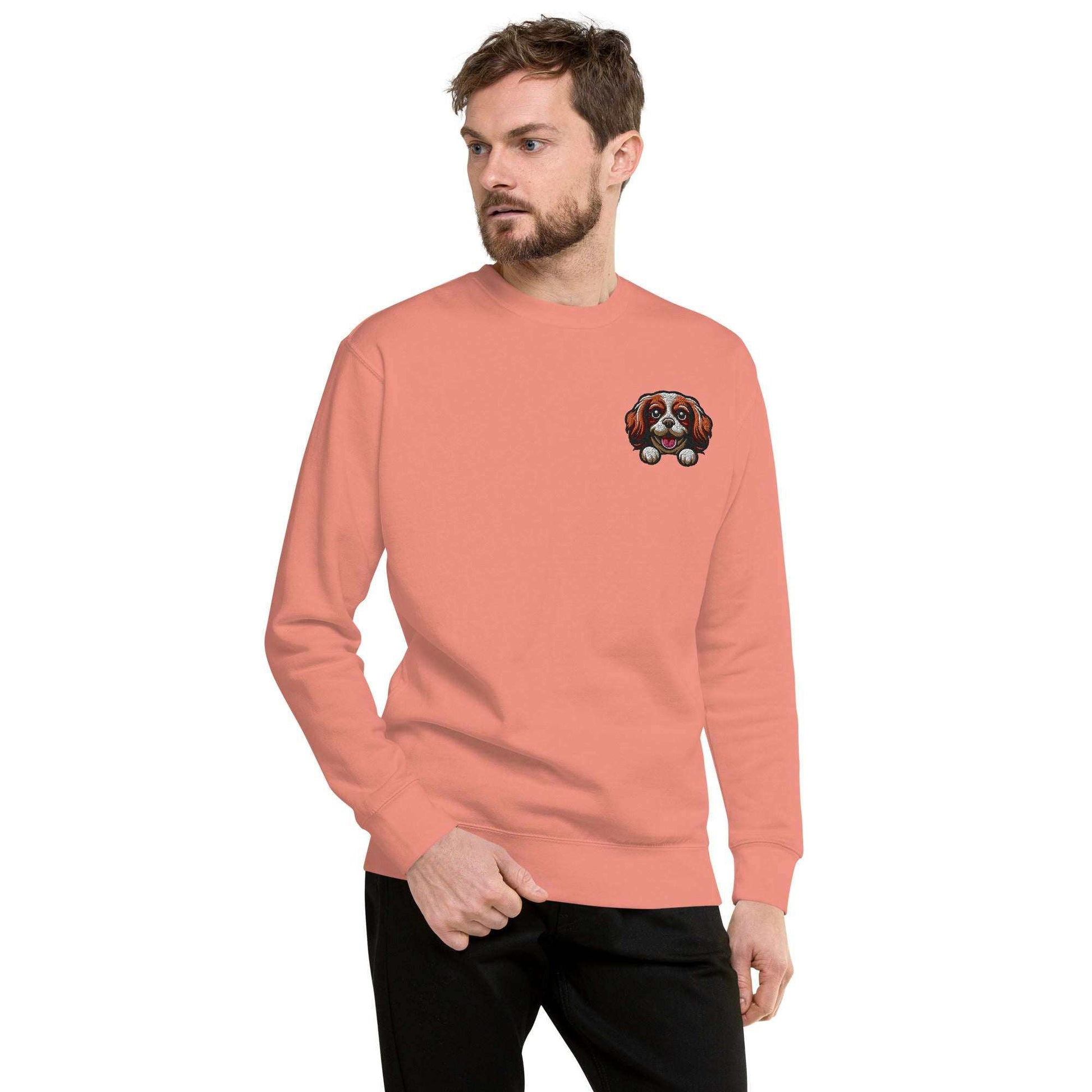 Man wearing coral sweatshirt with embroidered Cavalier King Charles Spaniel dog face on chest
