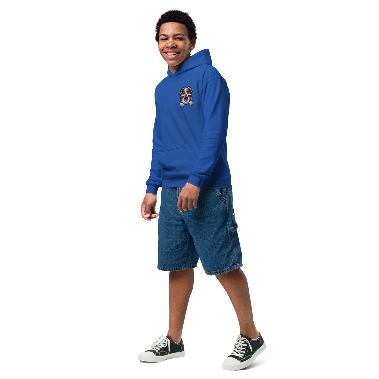 Youth unisex blue hoodie with detailed Australian Shepherd dog embroidery, paired with denim shorts and sneakers, modeled by a smiling young person.